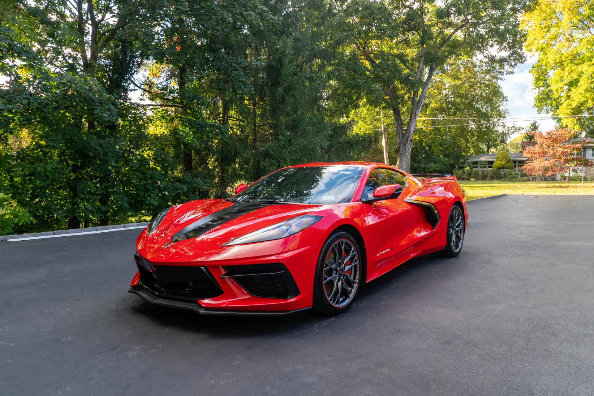 A red sports car is parked in a driveway surrounded by trees.