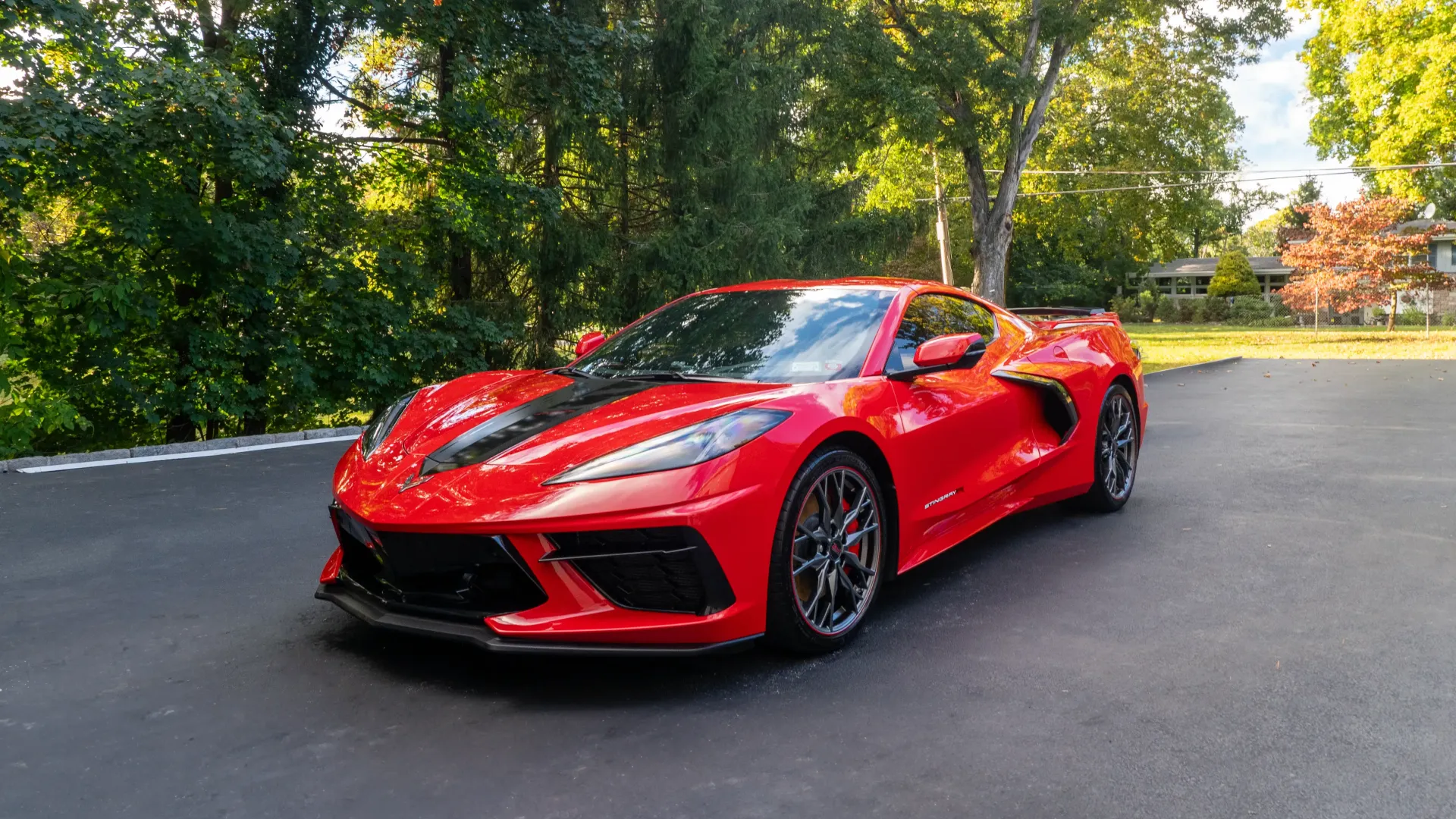 A red sports car is parked in a driveway next to trees.