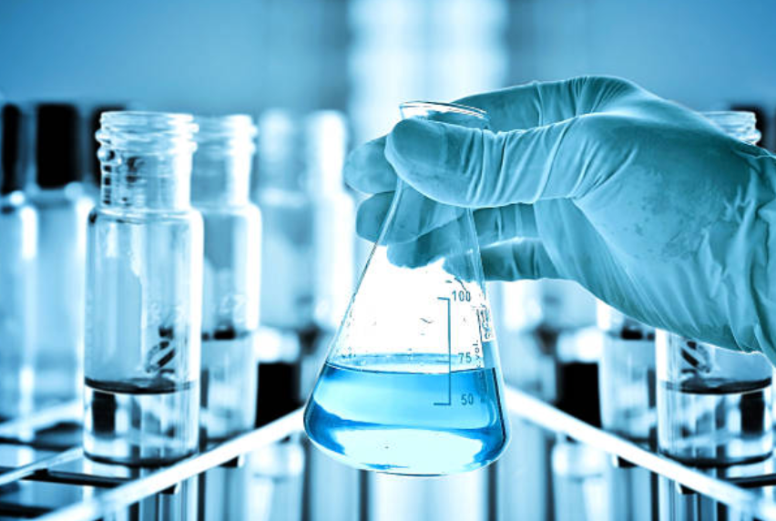 A person is holding a beaker with a blue liquid in it.
