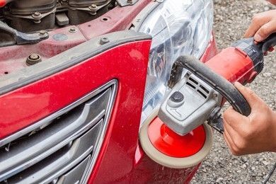 A person is polishing a red car 's headlight with a grinder.