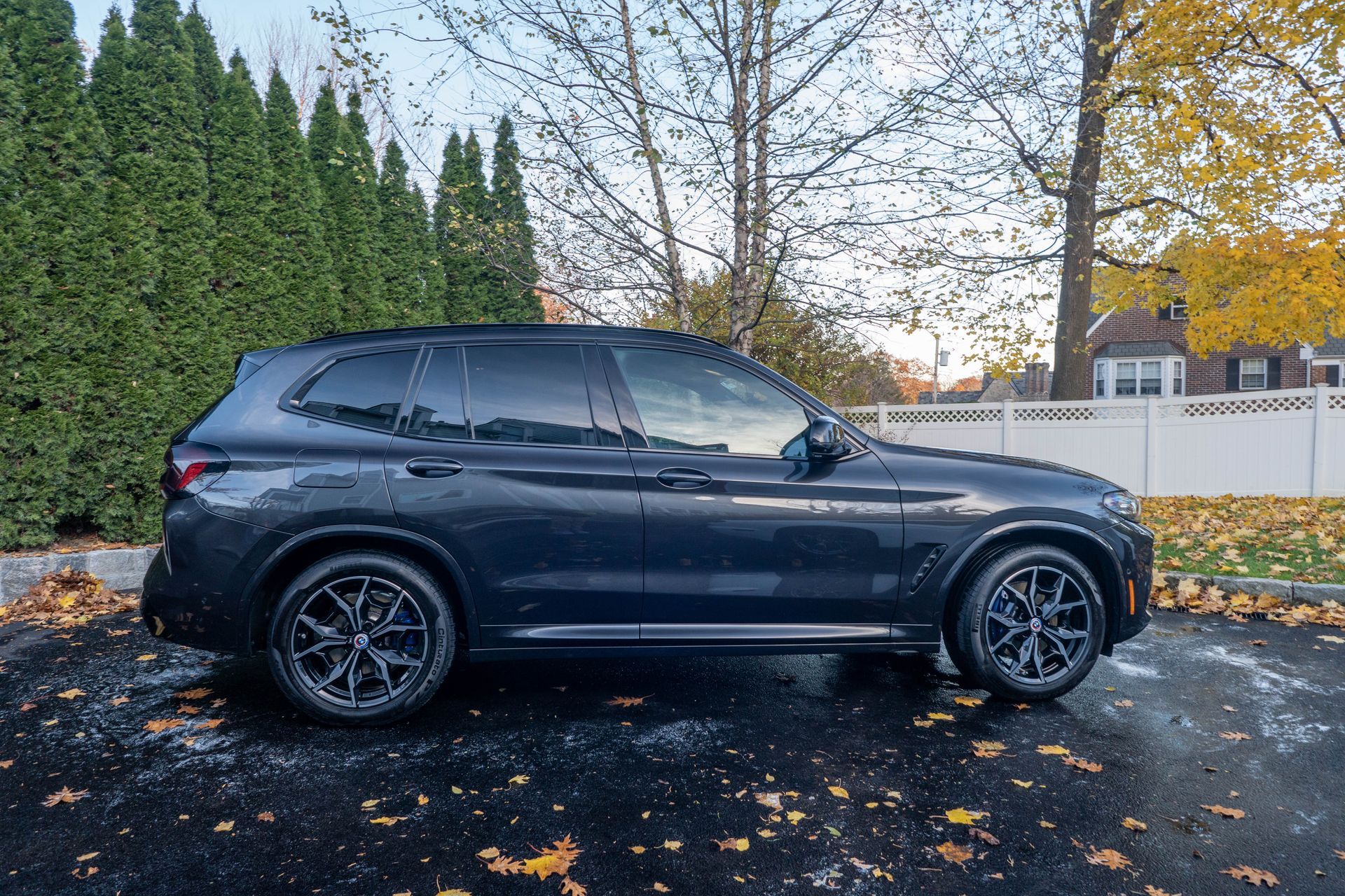 a black bmw x3 is parked in a driveway with leaves on the ground .