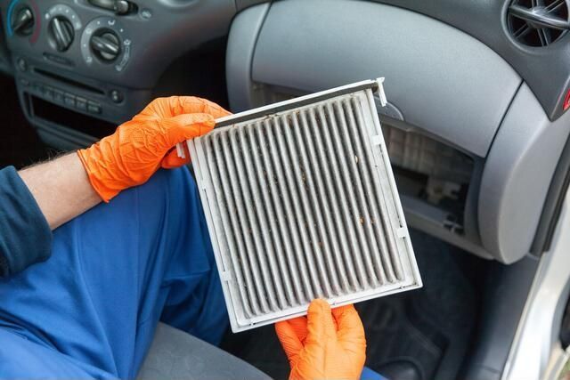 a man wearing orange gloves is holding a dirty air filter in a car .