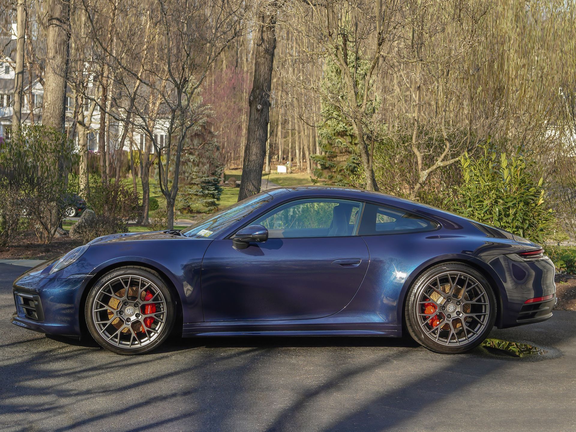 a blue porsche 911 is parked in a driveway next to trees .