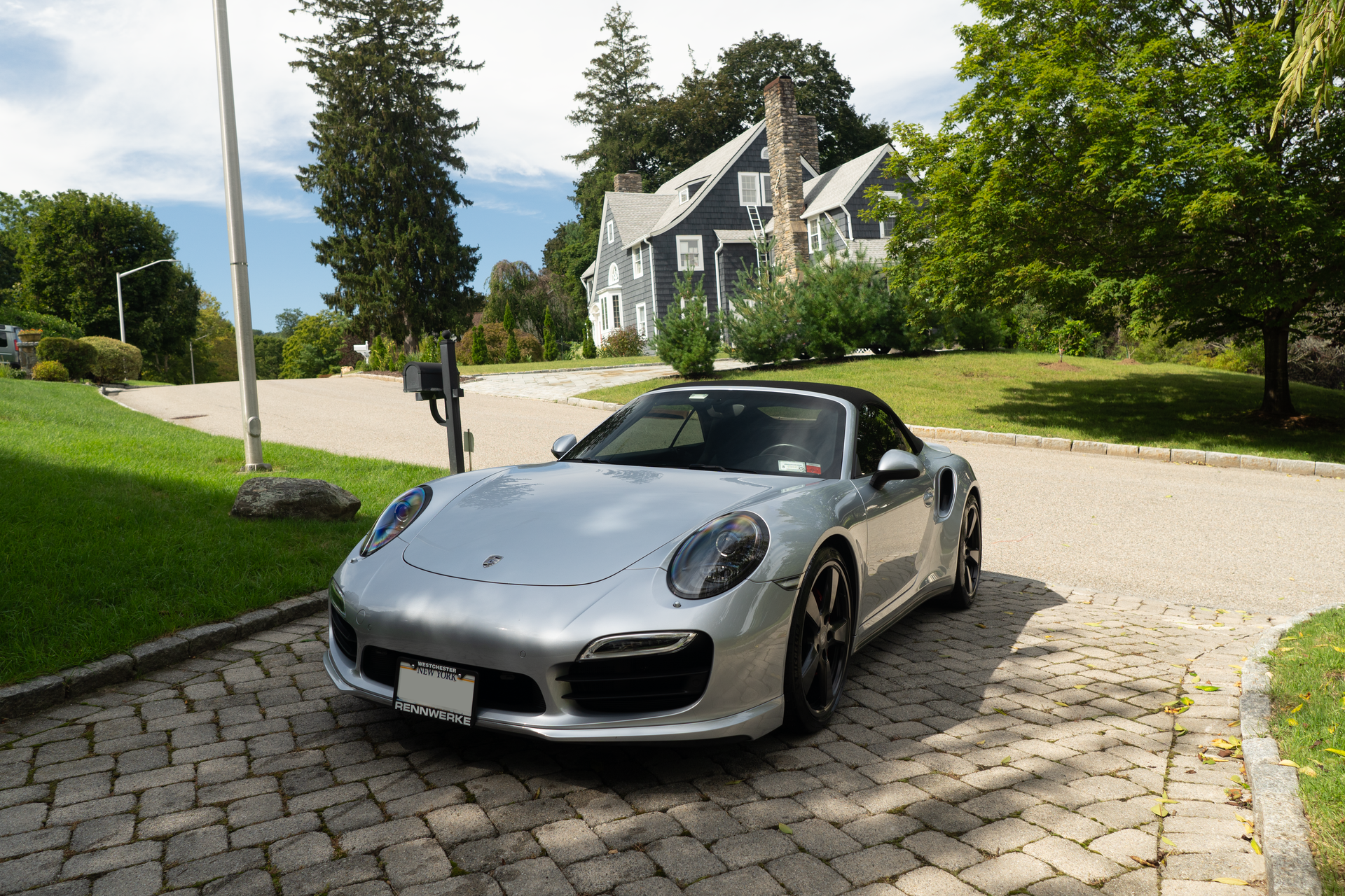 a silver sports car is parked on a brick driveway in front of a house