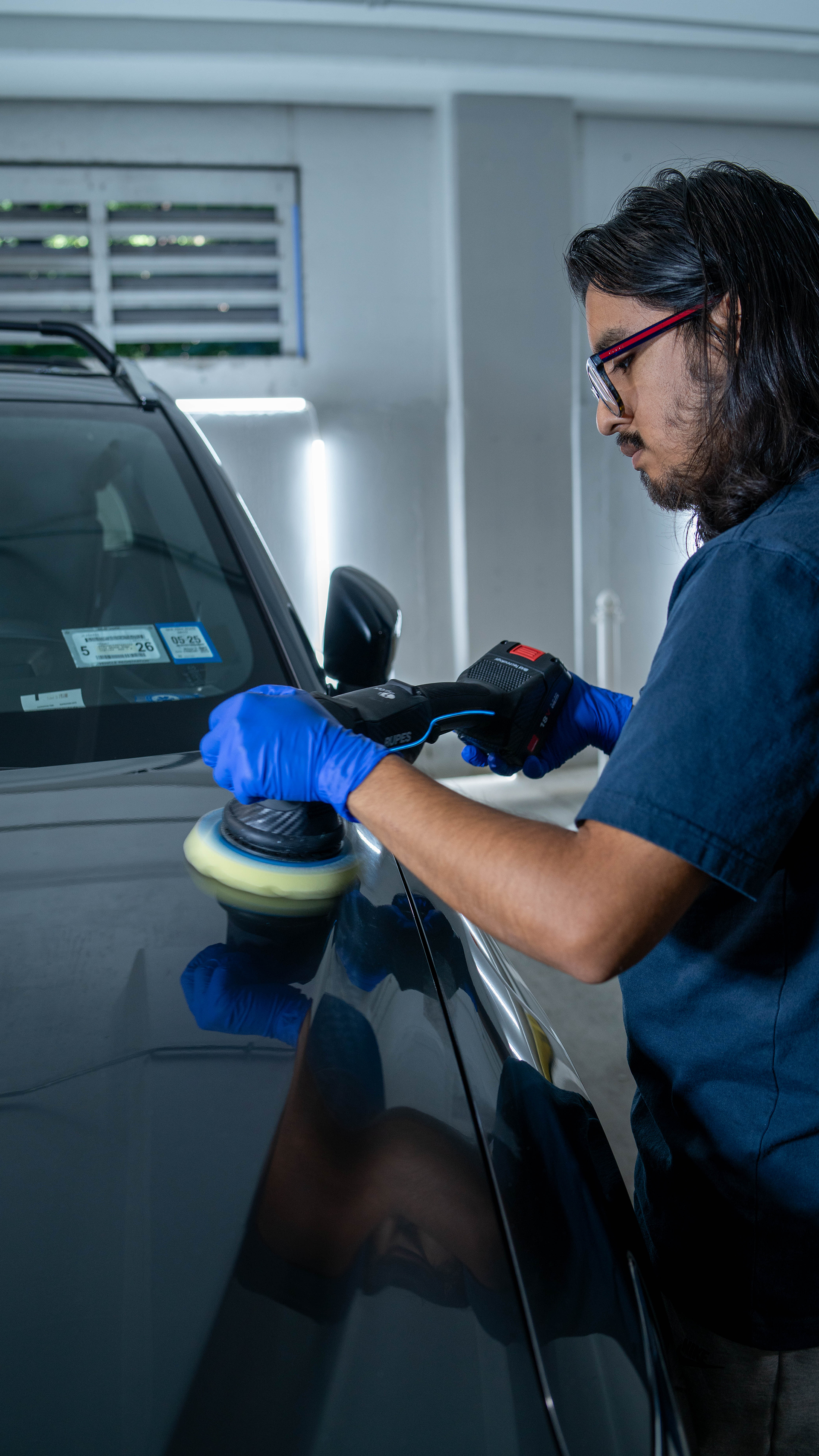 A person is holding a tool over a car hood.