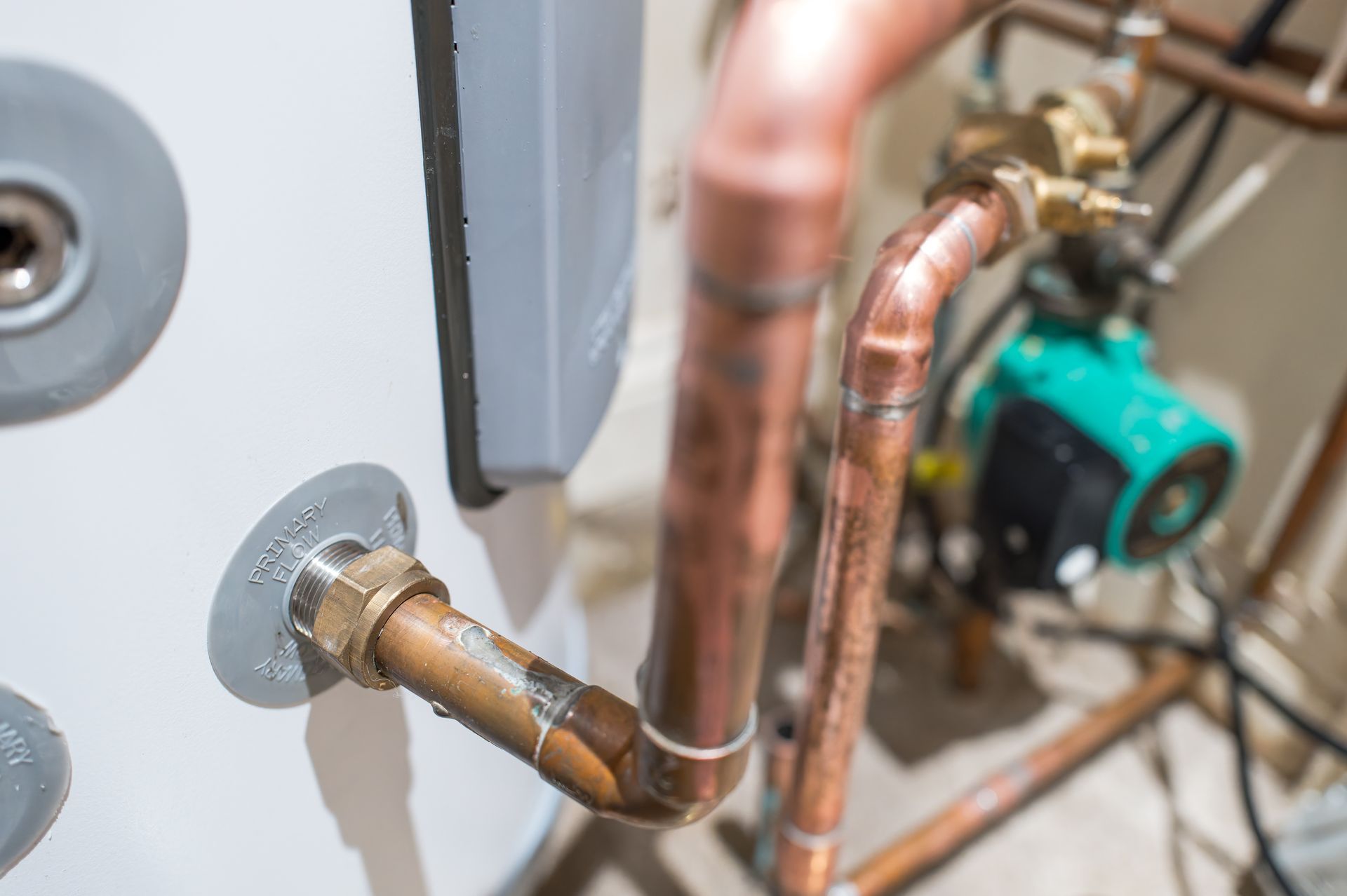Copper plumbing pipes and a green pump installed beside a gray wall. Copper plumbing pipes and a green pump installed beside a gray wall.