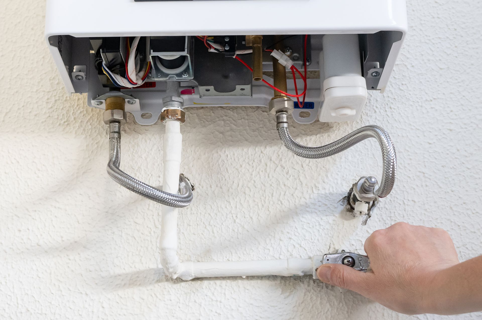 Hand turning a valve under a wall-mounted boiler with exposed plumbing and wires Hand turning a valve under a wall-mounted boiler with exposed plumbing and wires