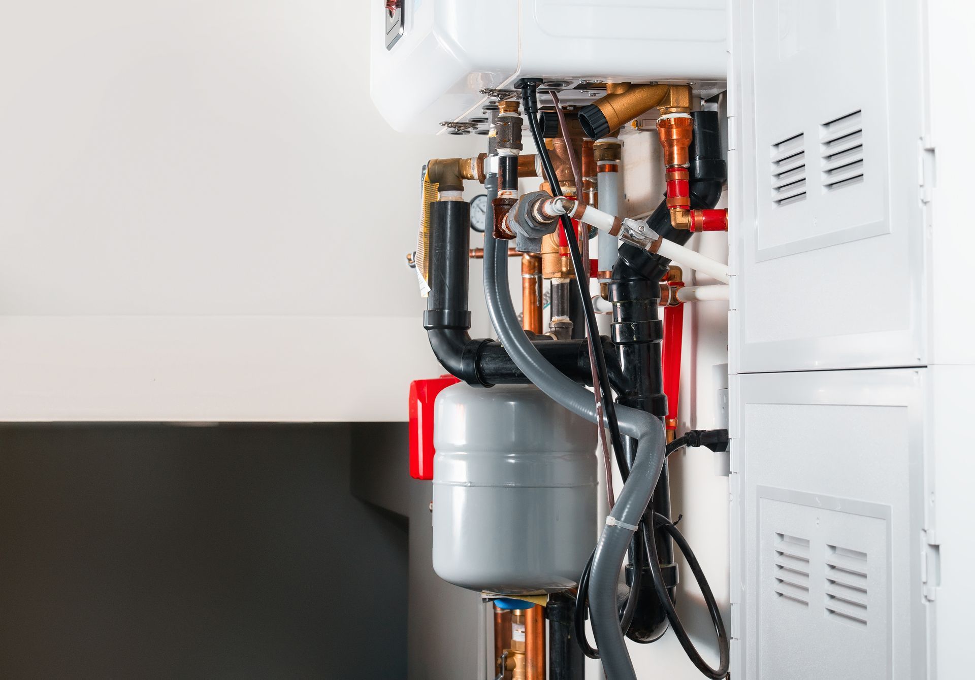 Wall-mounted boiler with exposed pipes and a gray expansion tank in a utility closet Wall-mounted boiler with exposed pipes and a gray expansion tank in a utility closet