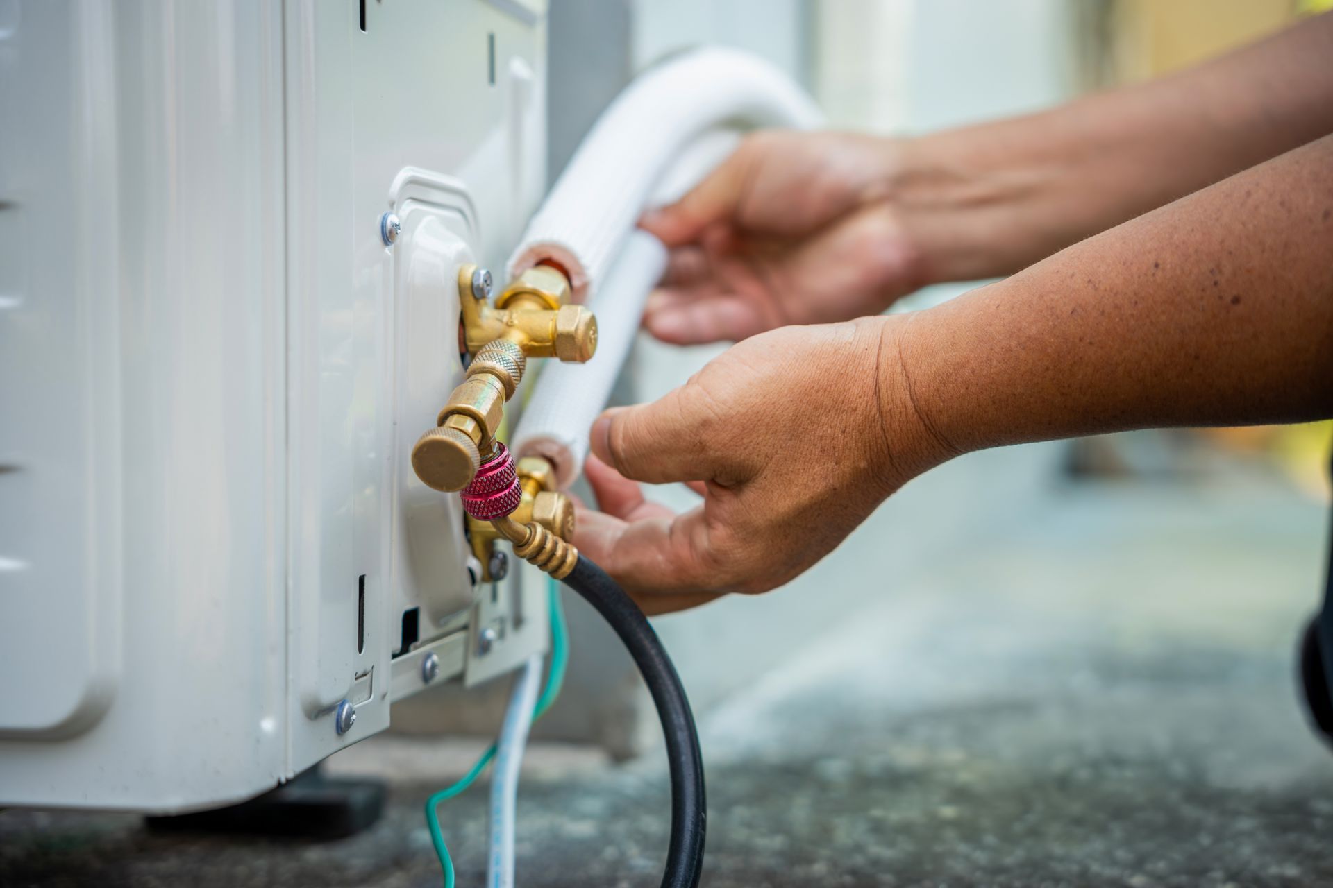 Hands connecting hoses to an outdoor air conditioner unit with brass fittings