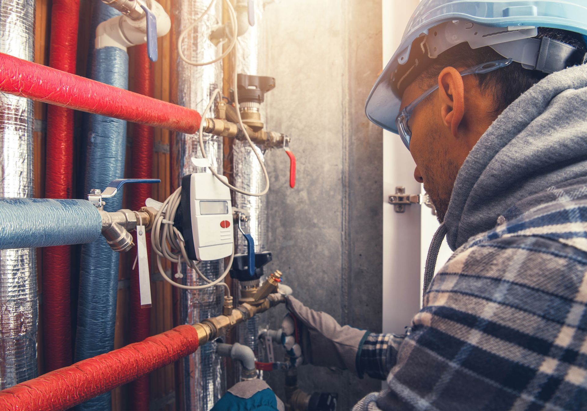 Technician inspecting pipes and valves in a boiler room, with red insulation and a hard hat