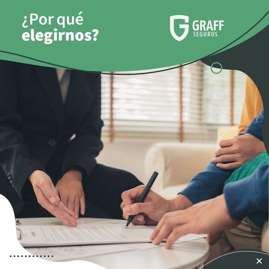 Una persona firma un documento en una mesa. Otra persona, vestida de traje, señala.