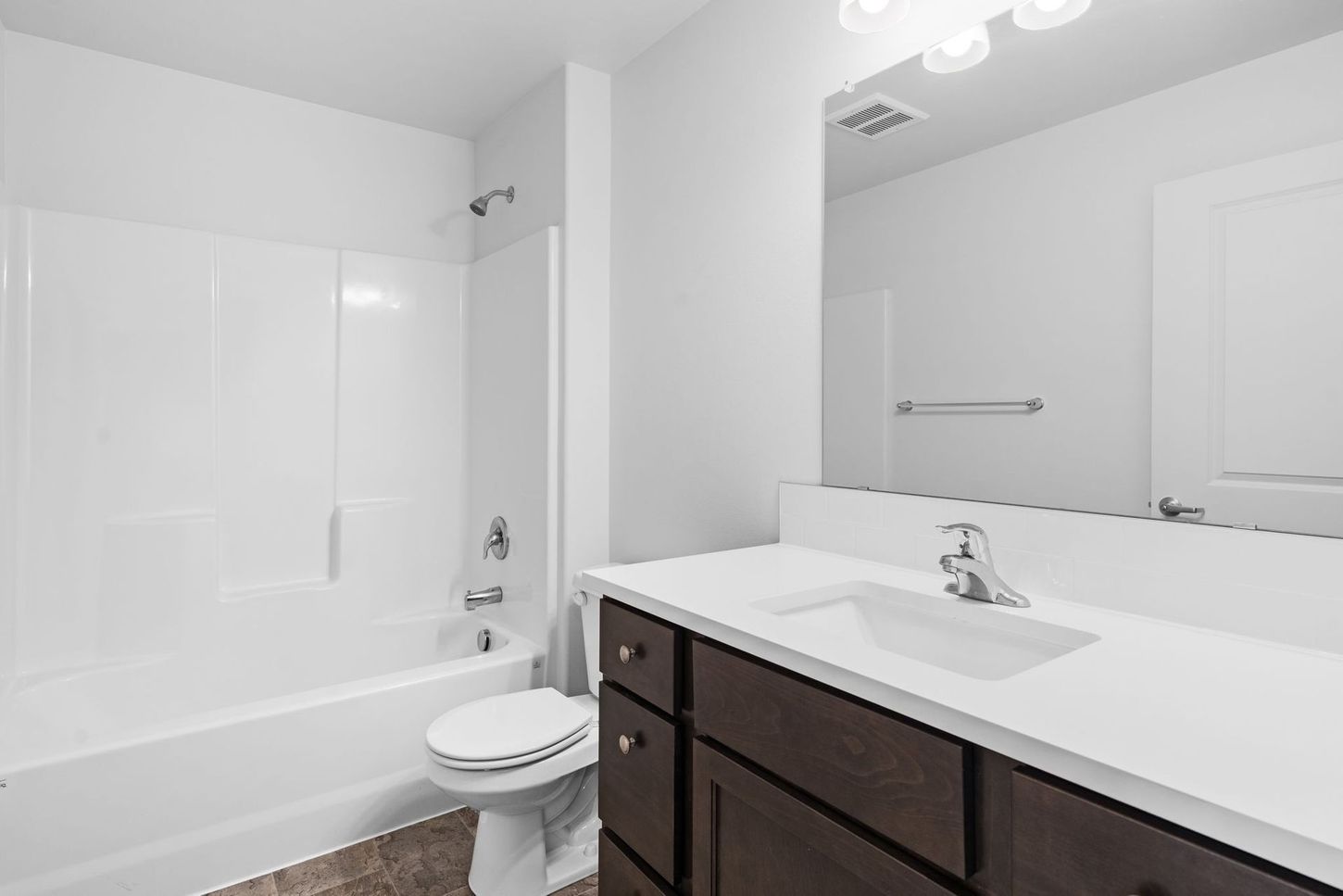Bright bathroom with white tub, toilet, large mirror, and dark vanity with sink.