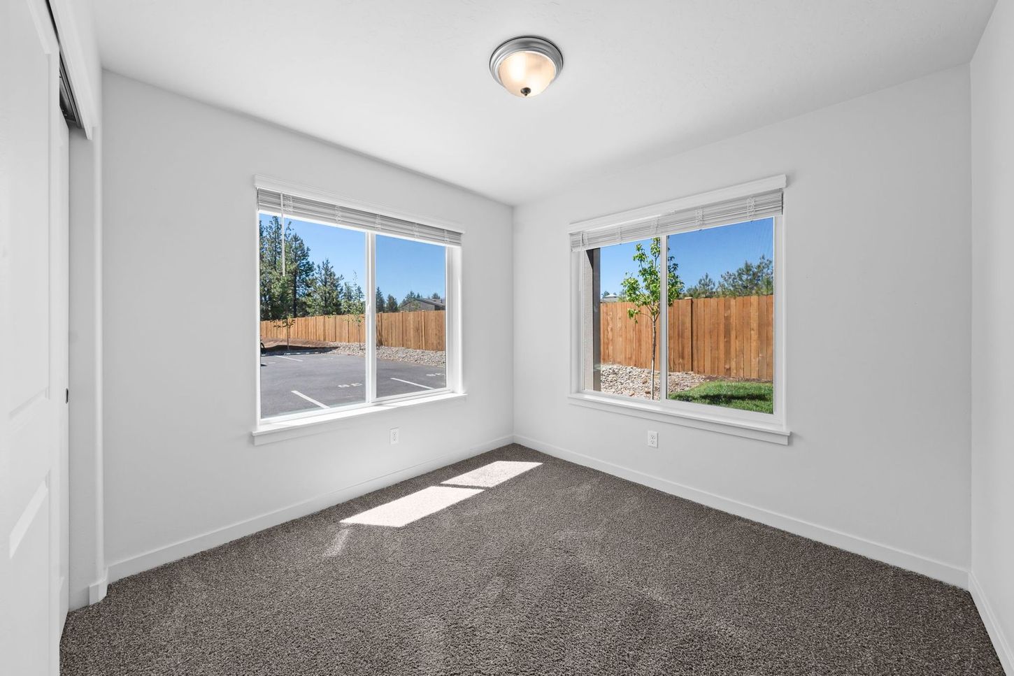 Empty white bedroom with gray carpet, two windows, and bright sunlight on the floor