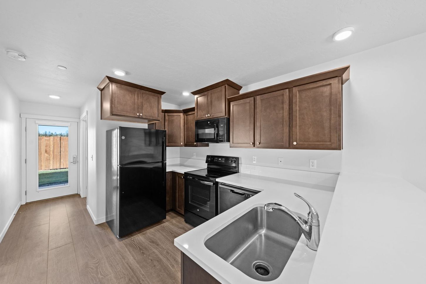 Bright kitchen with wooden cabinets, black appliances, and a white sink counter.