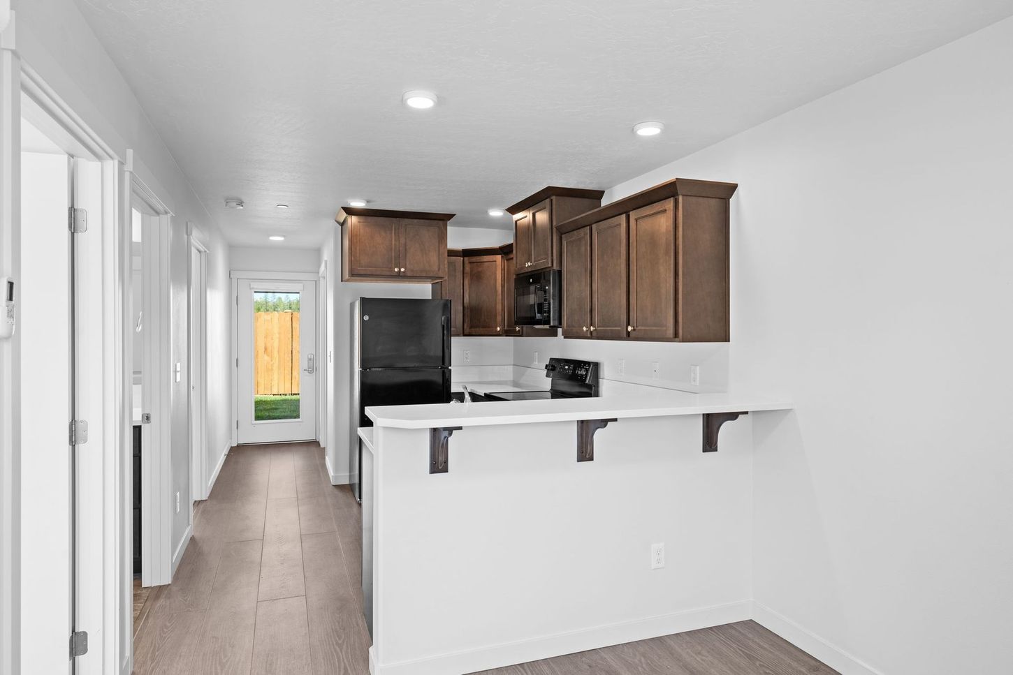 Bright kitchen and hallway with dark wood cabinets, white countertops, and light flooring