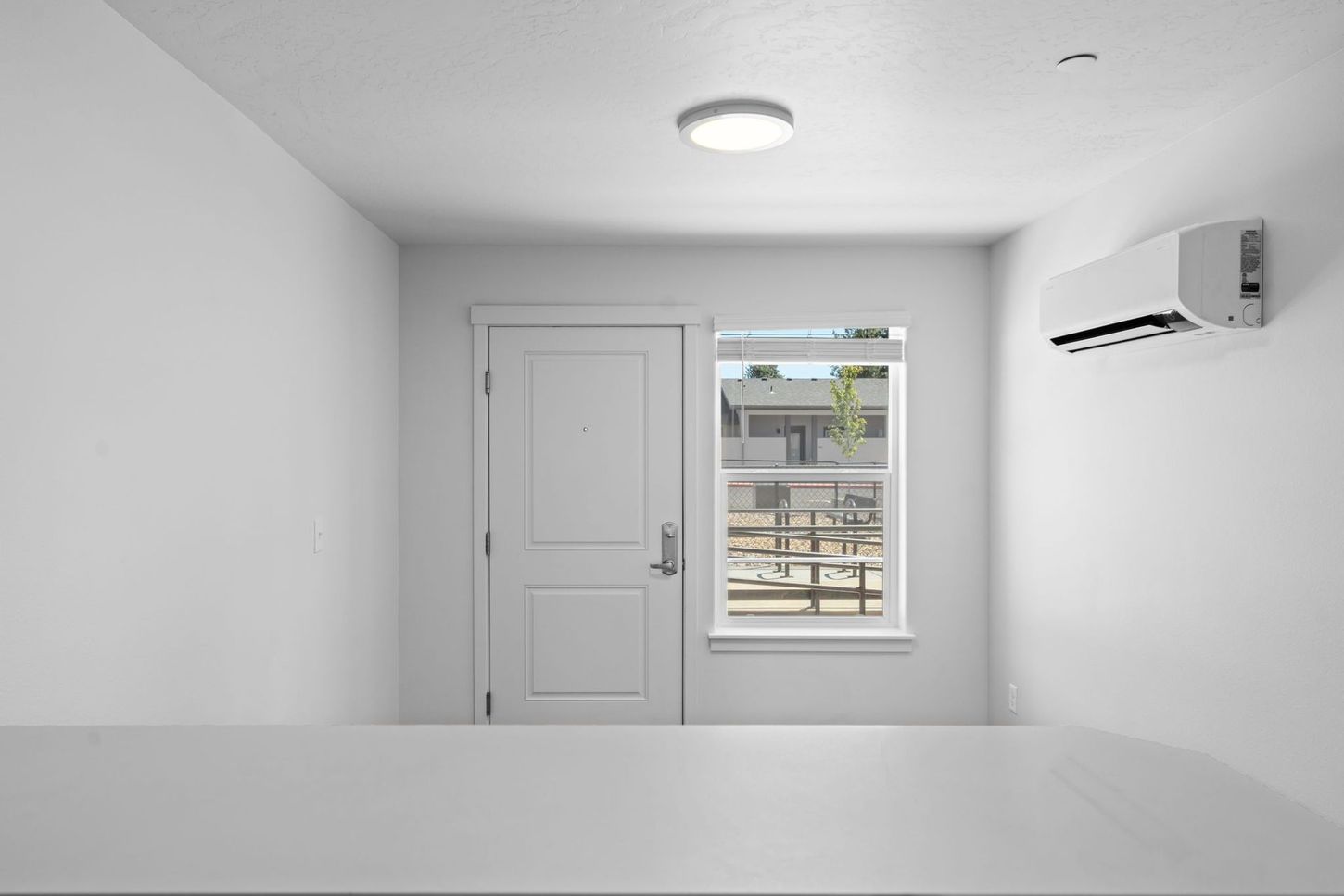 Minimal white room with a door, window, ceiling light, and wall-mounted air conditioner.