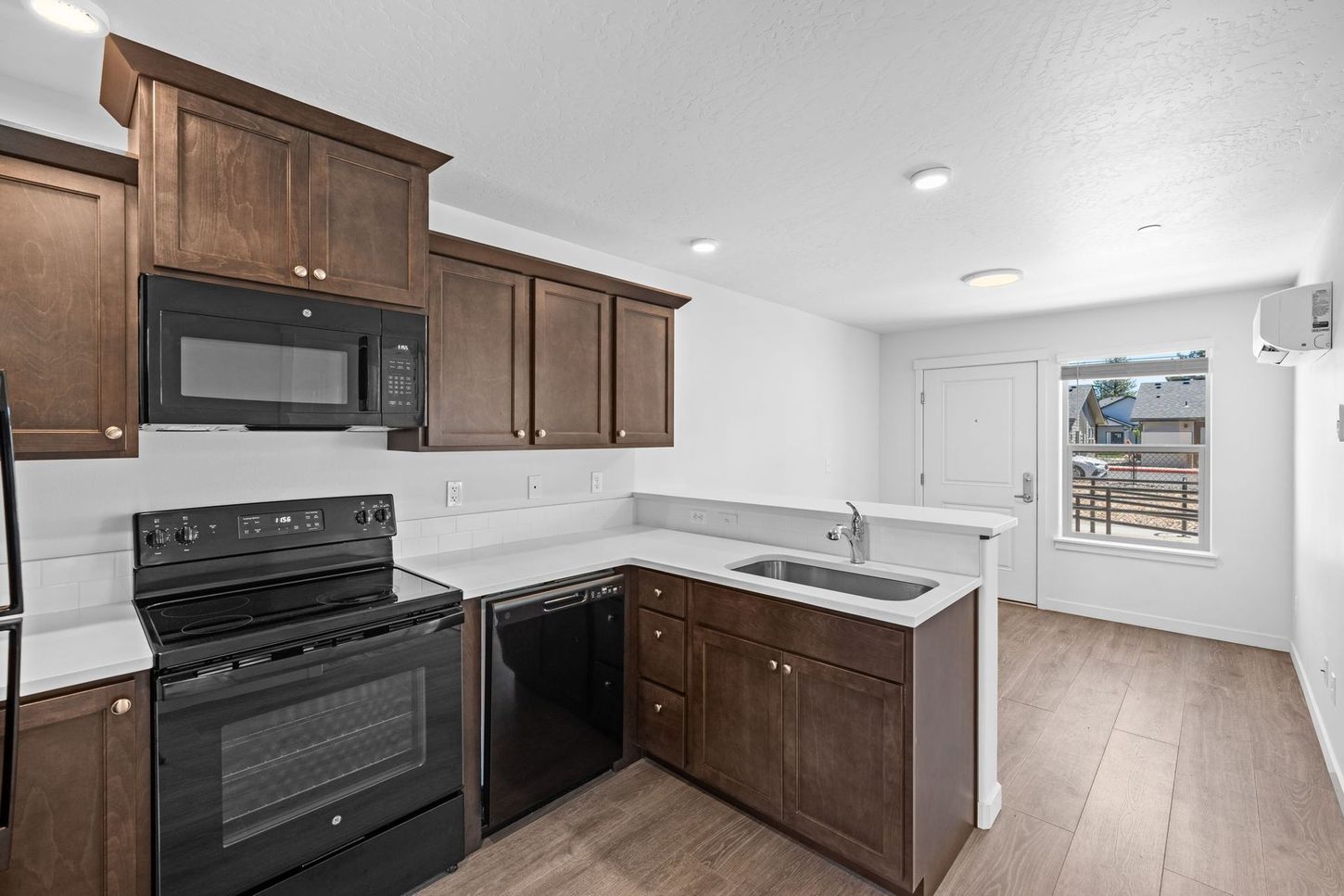 Empty kitchen with dark wood cabinets, black appliances, white countertops, and light wood floors