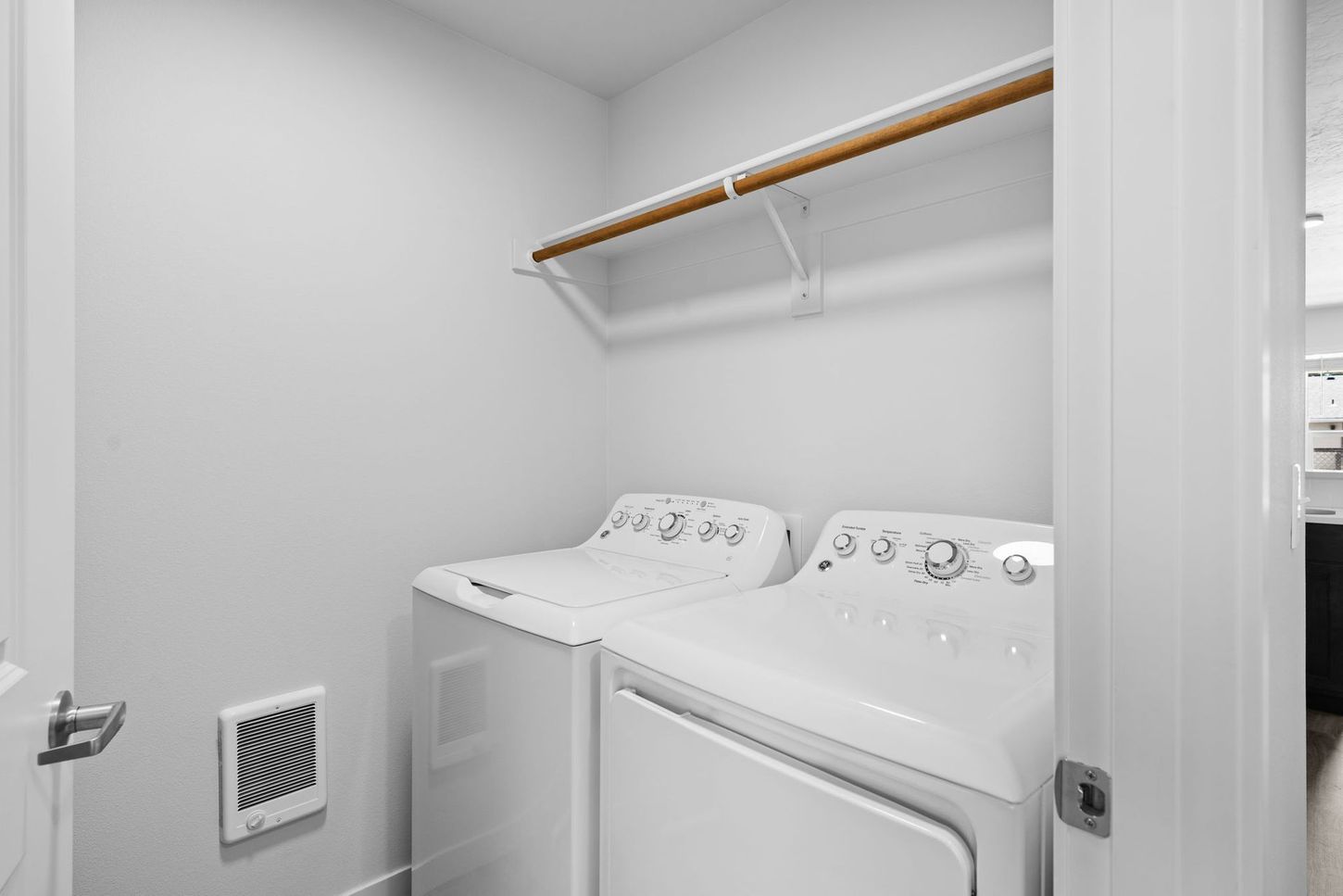 Small laundry room with a washer, dryer, white walls, and a wooden shelf above.