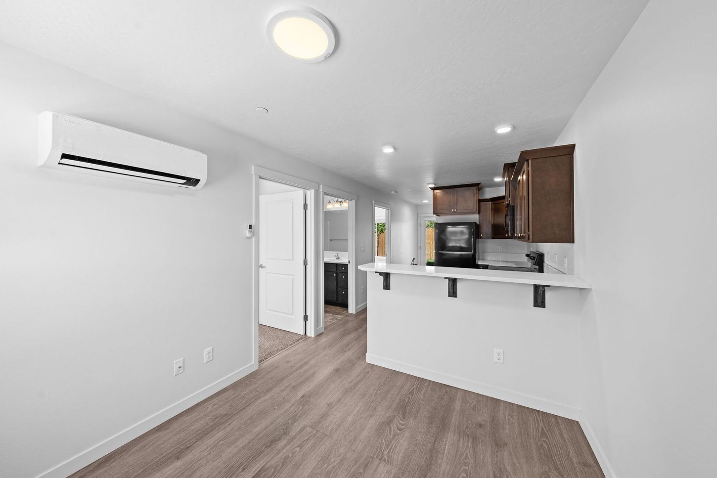 Modern apartment living room with white walls, wood floors, kitchen bar, and wall-mounted air conditioner