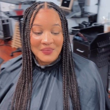 A person with long, dark, box-braided hair wearing a black salon cape in a salon setting.