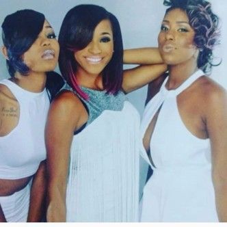 Three people with diverse hairstyles pose together against a white background, all wearing white outfits.