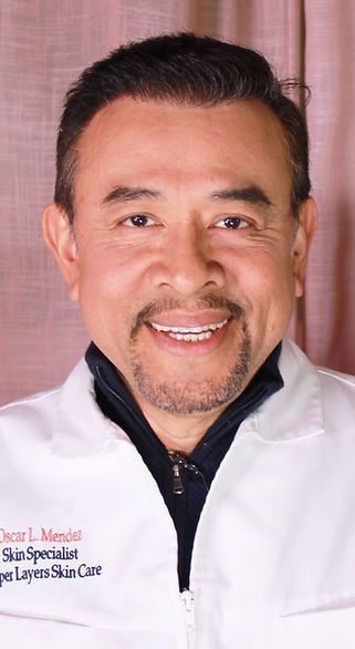 A man with a beard is wearing a white lab coat and smiling.