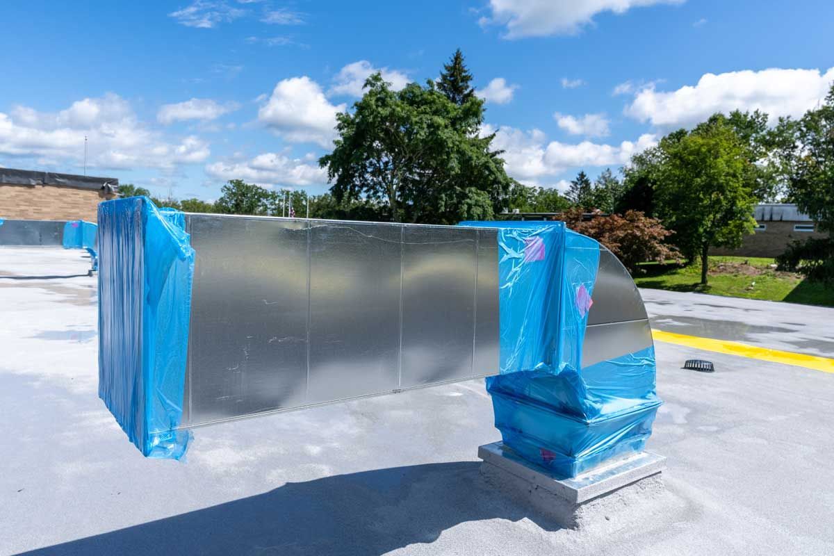 Metal equipment wrapped in blue plastic on a rooftop under a sunny sky