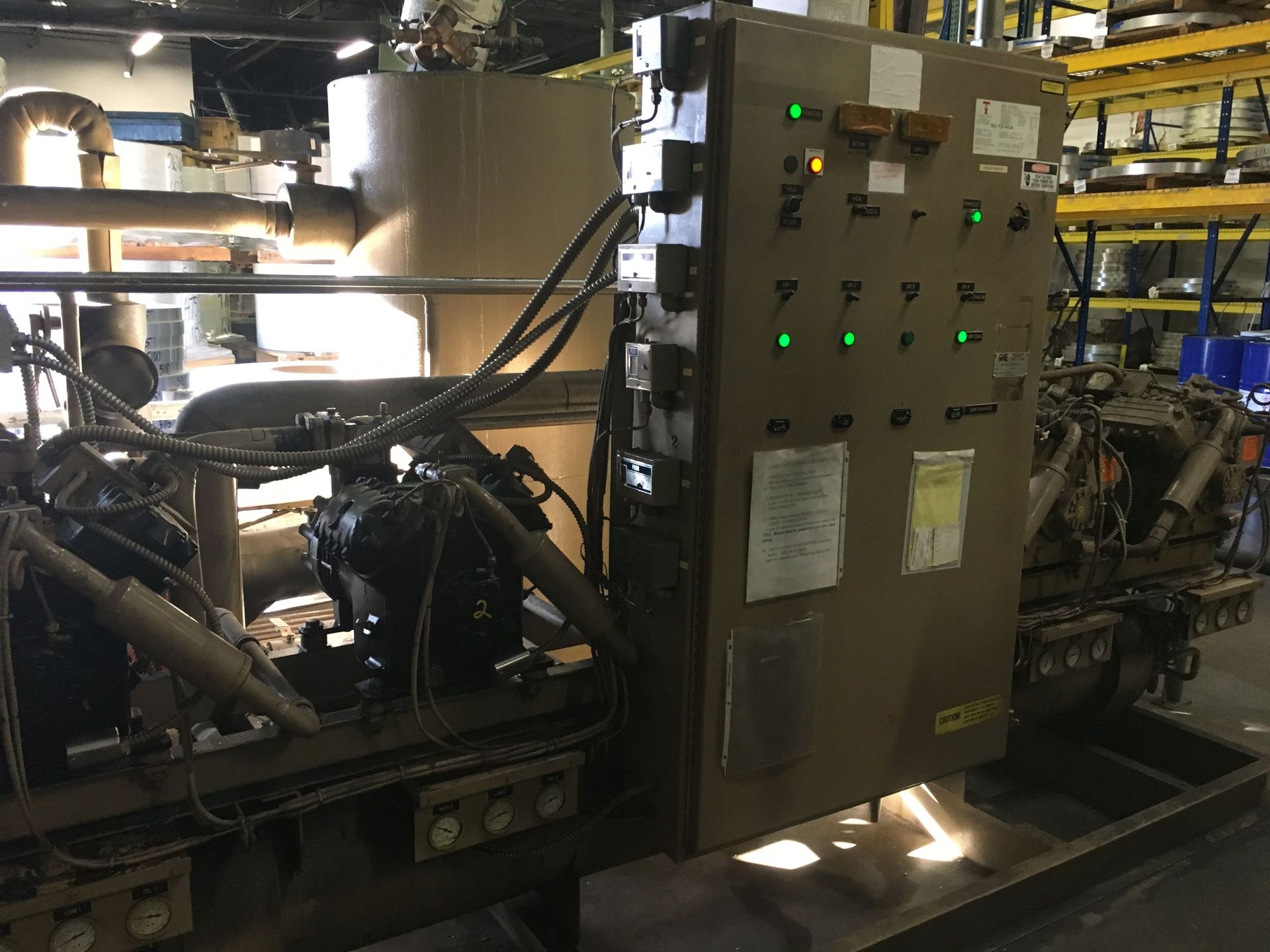 Industrial refrigeration unit featuring a brown control panel with illuminated green status lights in a warehouse setting.
