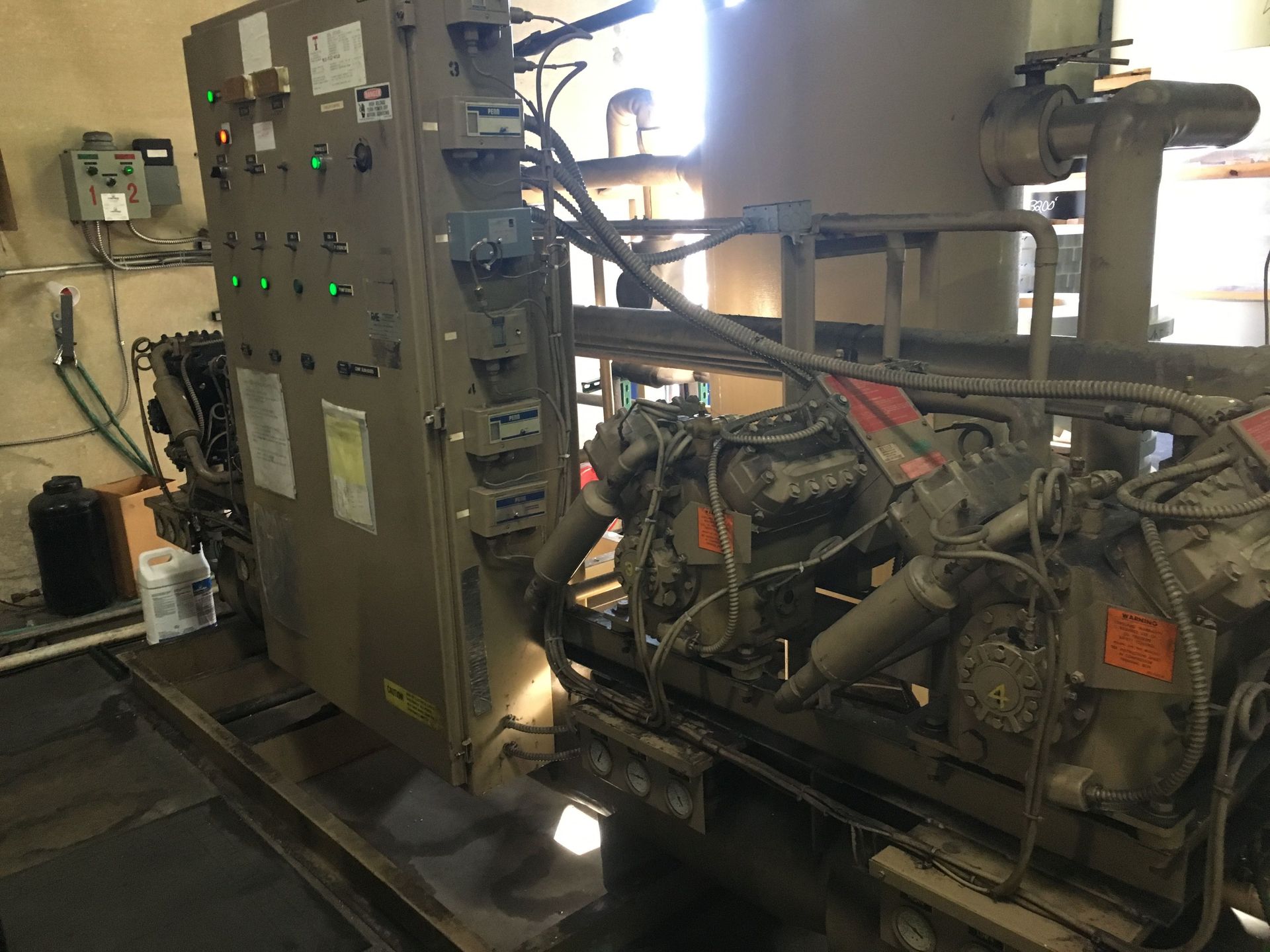 An industrial control panel connected to a set of heavy-duty mechanical compressors in a utility room setting.