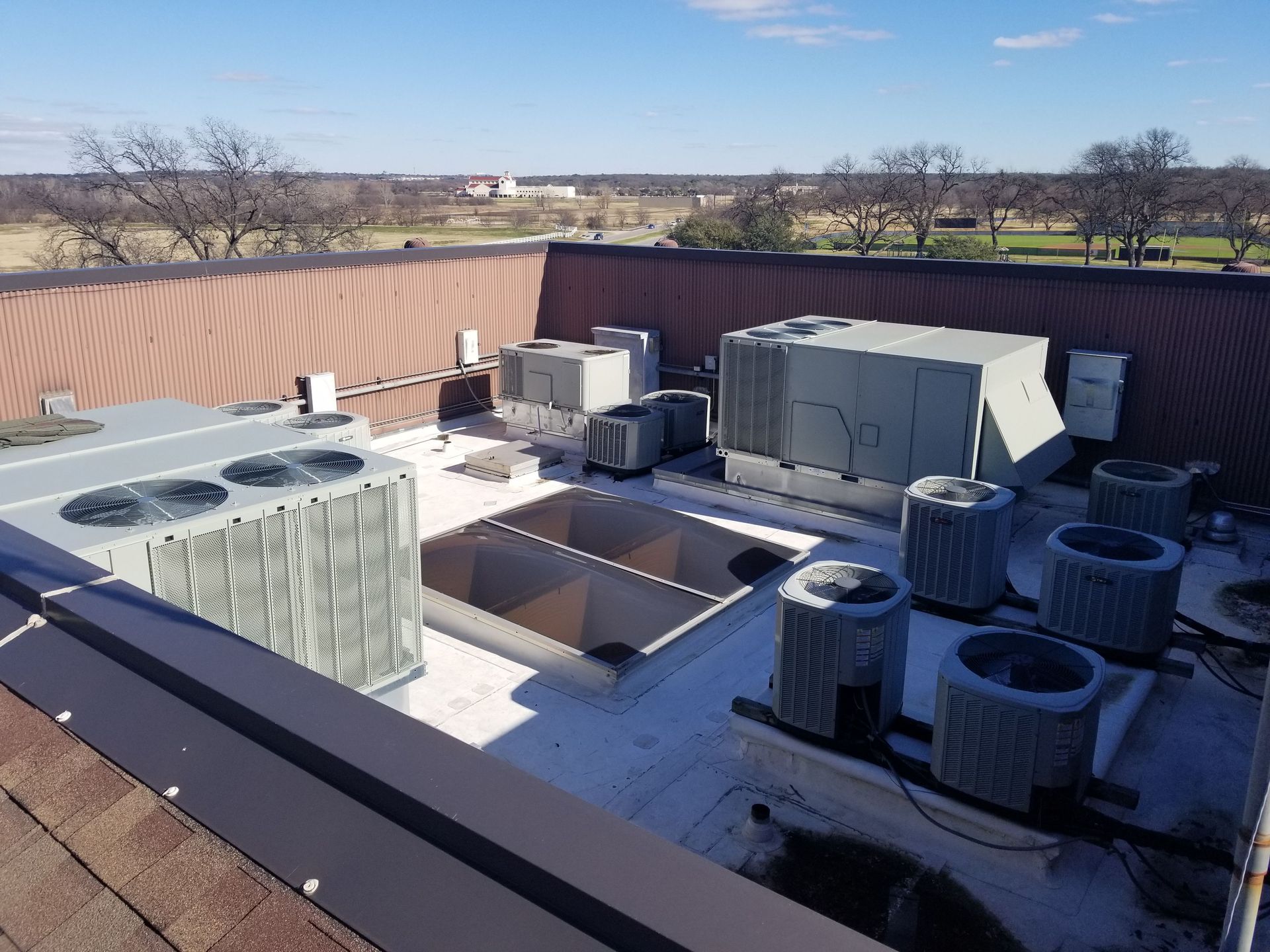 Commercial rooftop with multiple HVAC condenser units and a square roof hatch under a clear blue sky.
