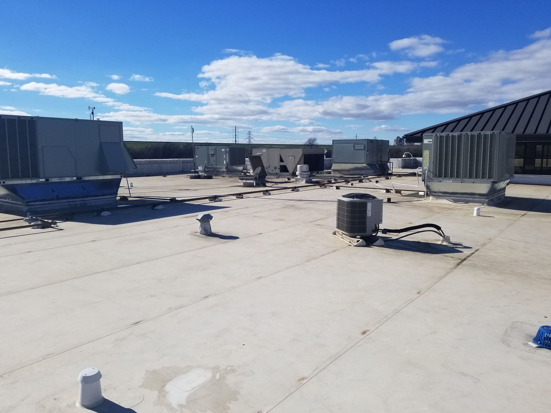 A flat commercial roof under a blue sky, featuring multiple HVAC units and ventilation equipment.