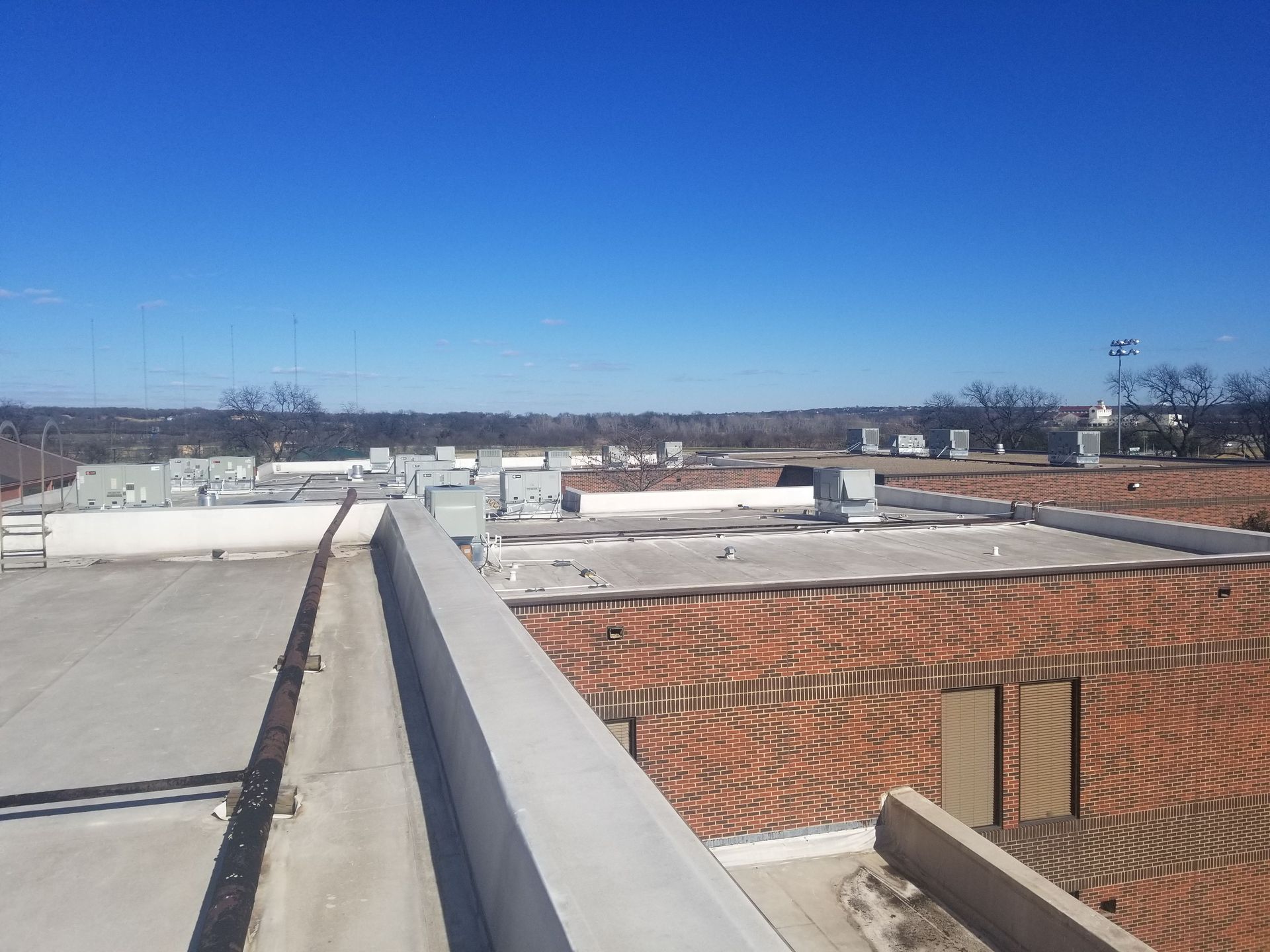 A high-angle view of a flat commercial roof with HVAC units under a clear blue sky.
