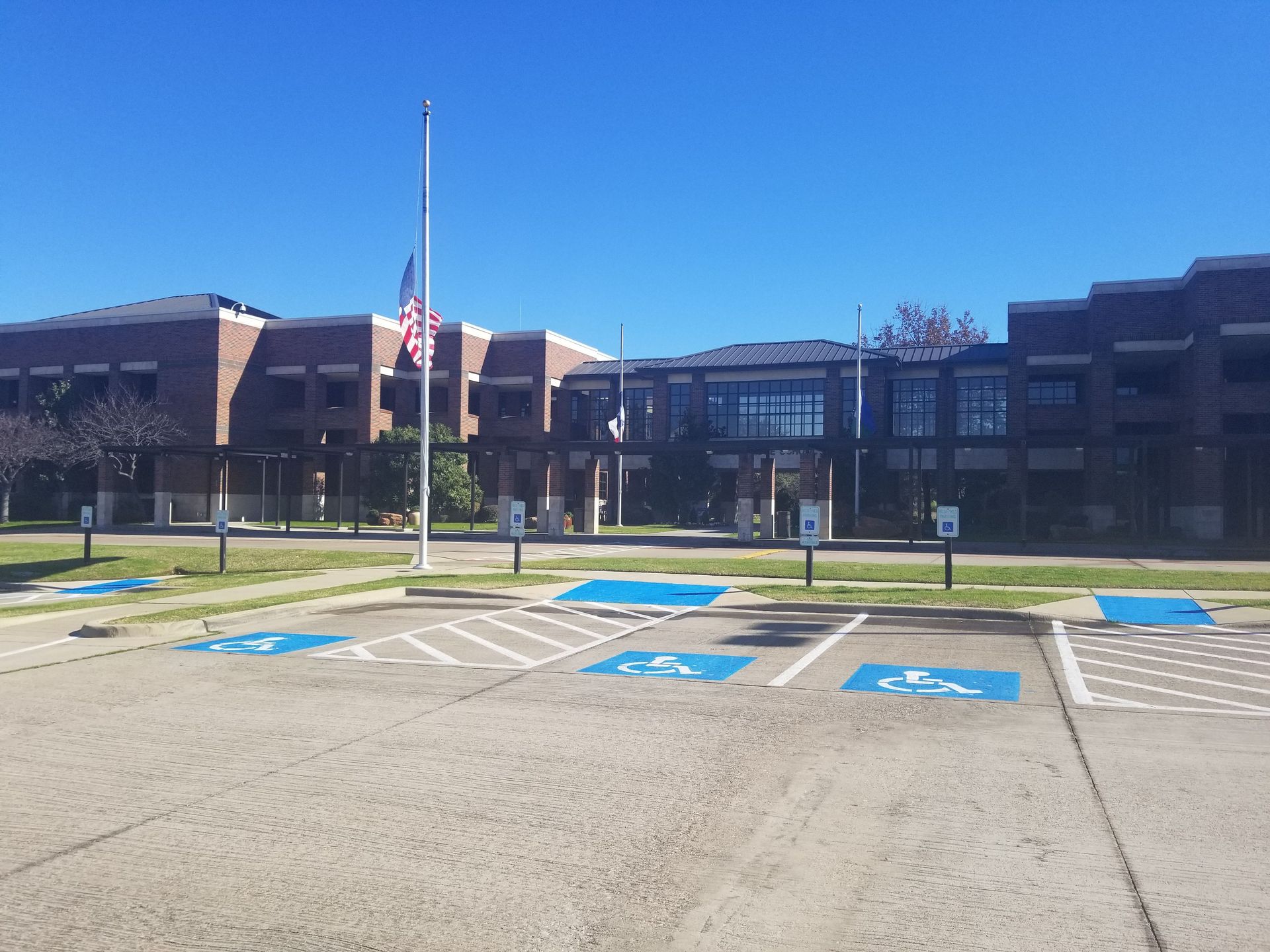 A low-angle view of a brick school building under a clear blue sky, with a parking lot featuring handicap-accessible spots.
