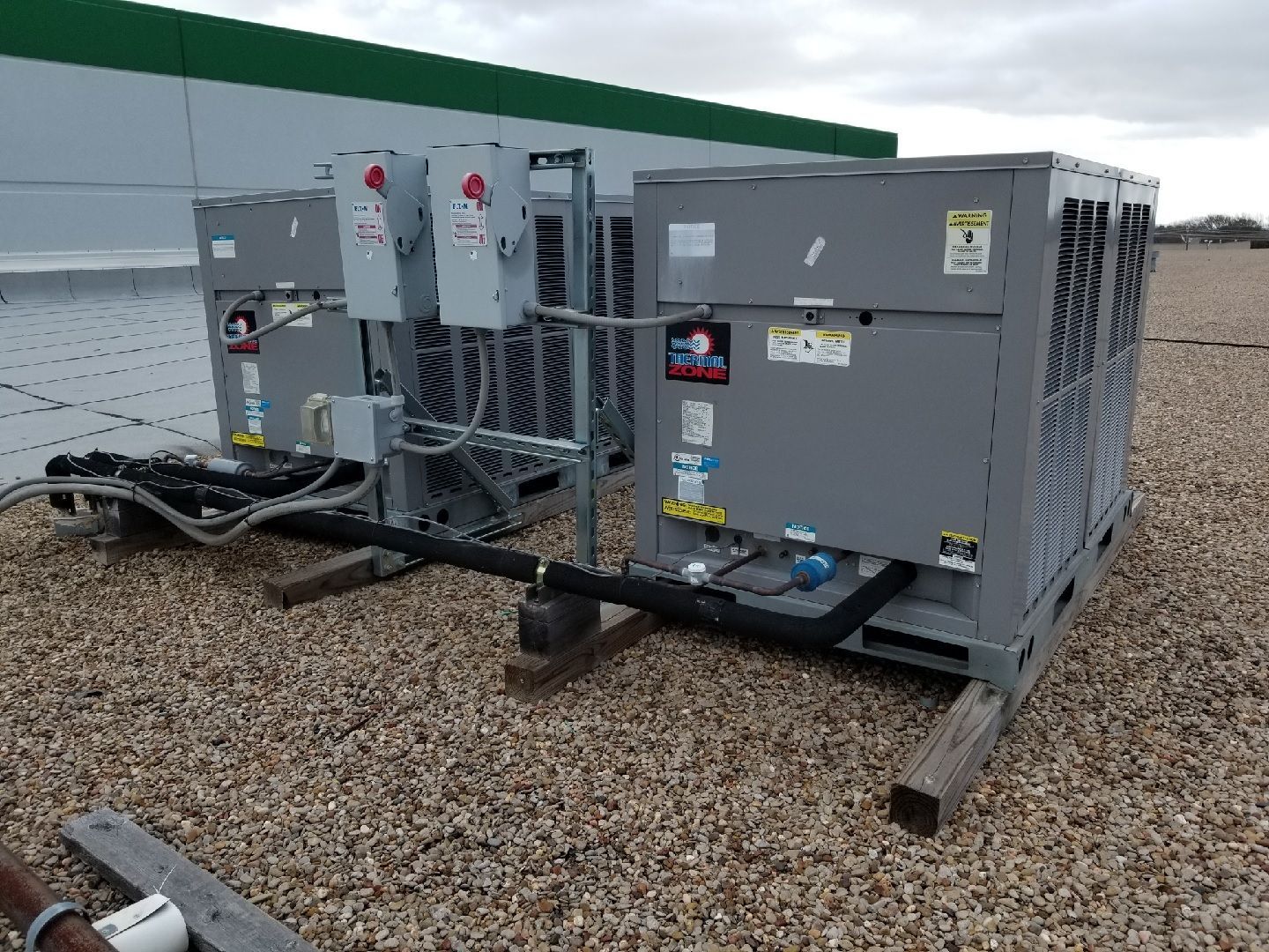Two gray HVAC rooftop units positioned on a graveled roof surface with electrical disconnect boxes and conduits attached.