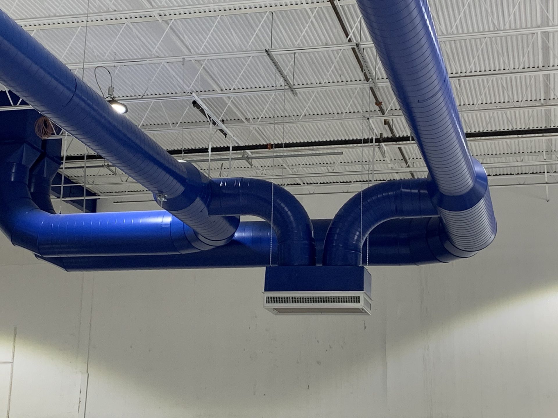 Blue ventilation ducts suspended from a white ceiling, connecting to a central rectangular air diffuser.