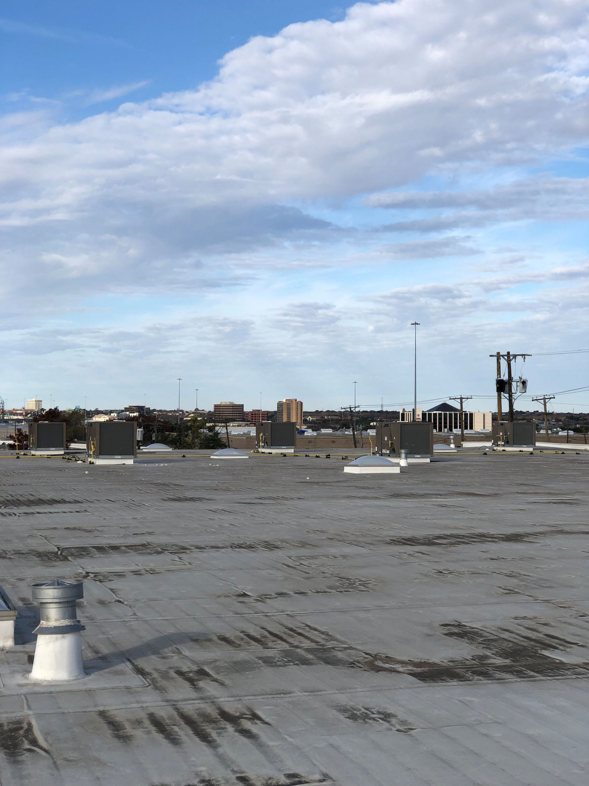 A flat commercial building roof with HVAC units and a vent, under a blue sky with soft, scattered clouds.