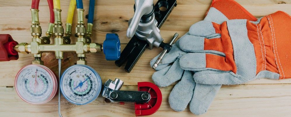 HVAC manifold gauges, a pipe cutter, and work gloves resting on a wooden surface.
