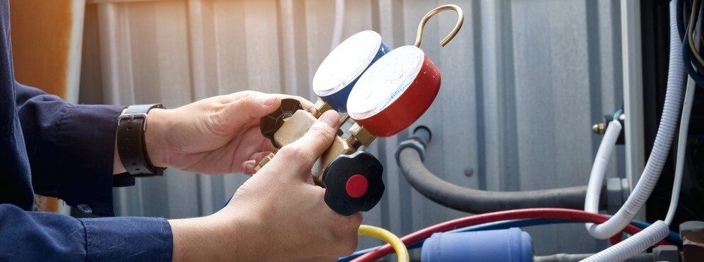 A technician holds a colorful HVAC manifold gauge set while repairing an outdoor air conditioning unit.