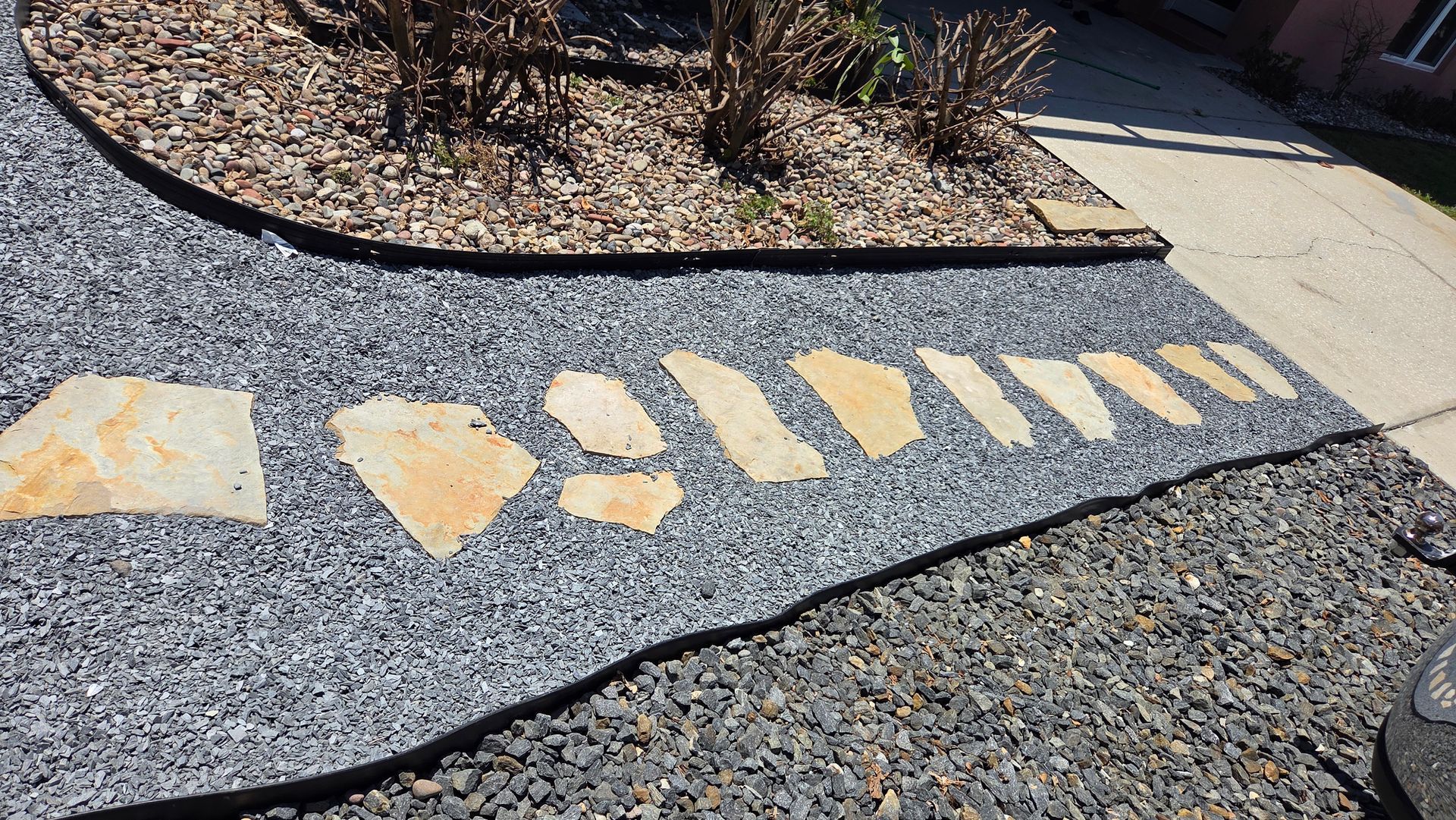 Yellow painted arrows and blocks on a gravel path beside a curb in a landscaped area