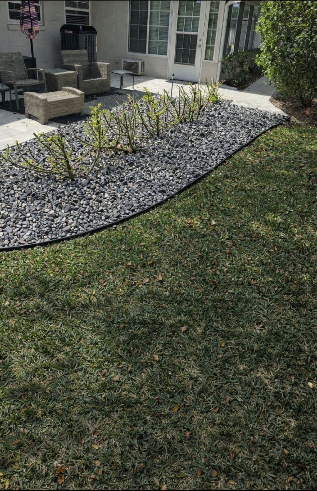 Landscape bed with small shrubs and gray rocks beside a house, bordered by green lawn