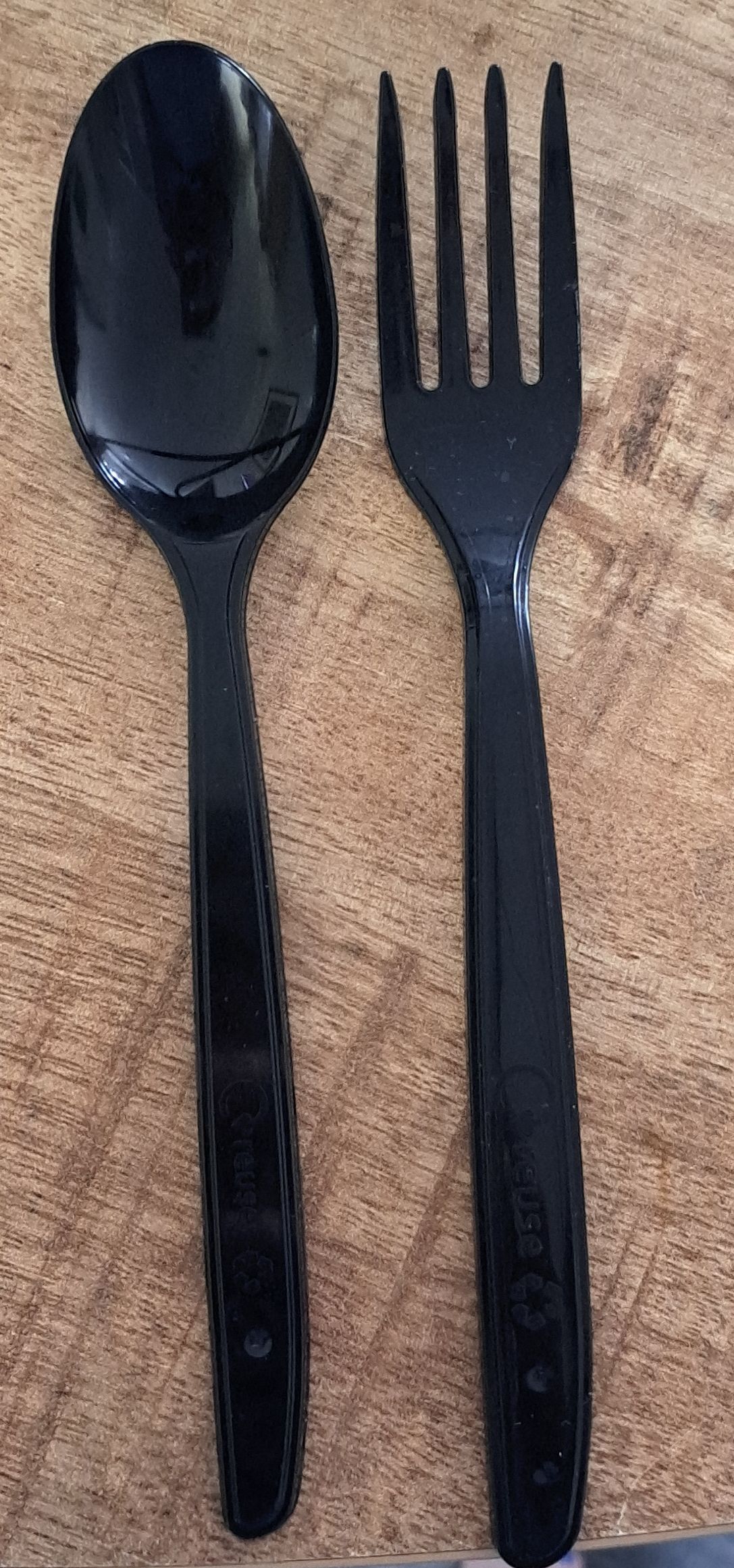 Zwarte plastic lepel en vork op een houten ondergrond.