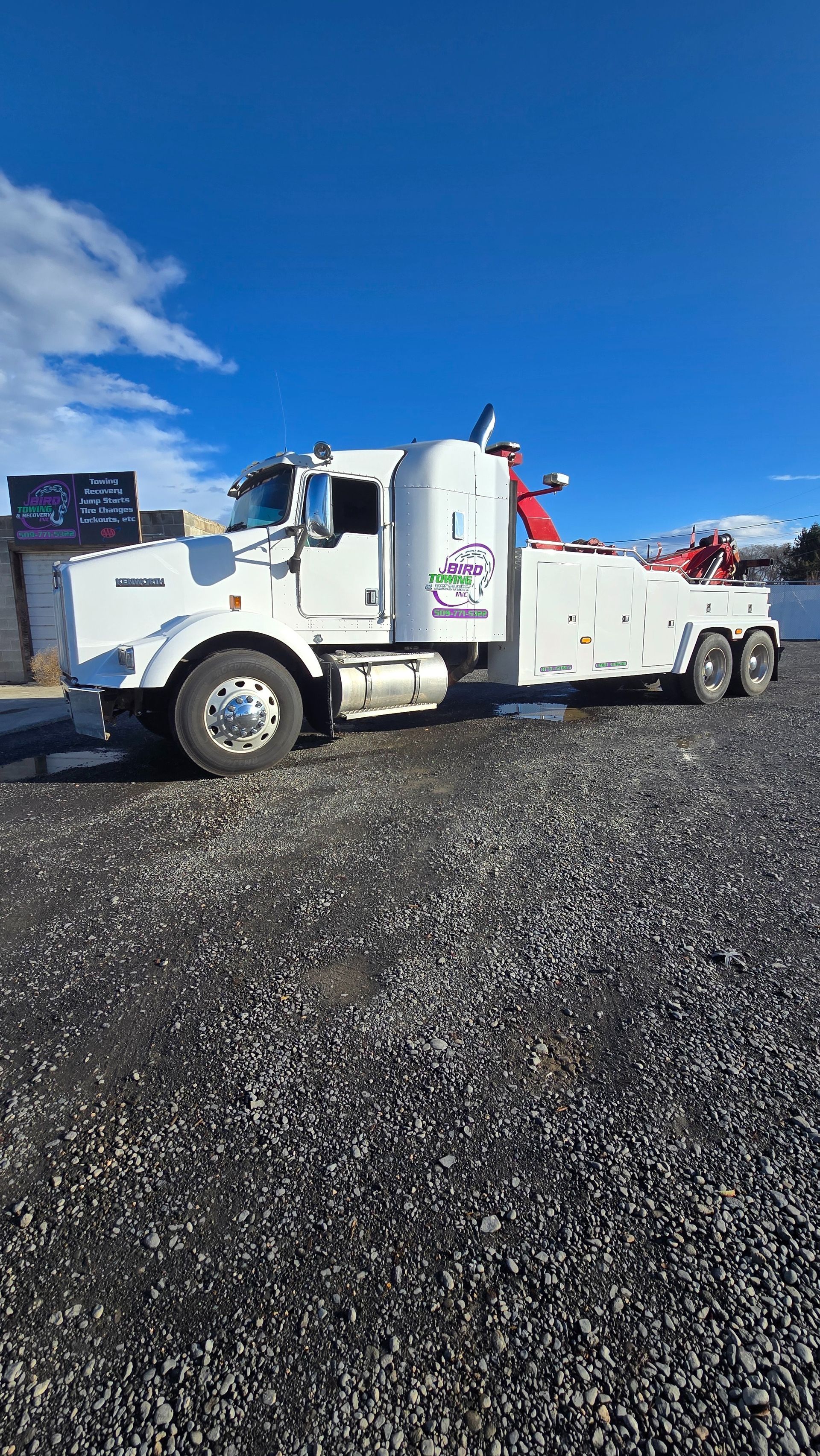 White tow truck parked on gravel under a bright blue sky.