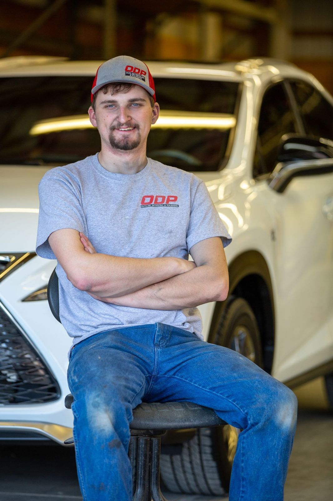 A man is sitting on a chair in front of a white car.