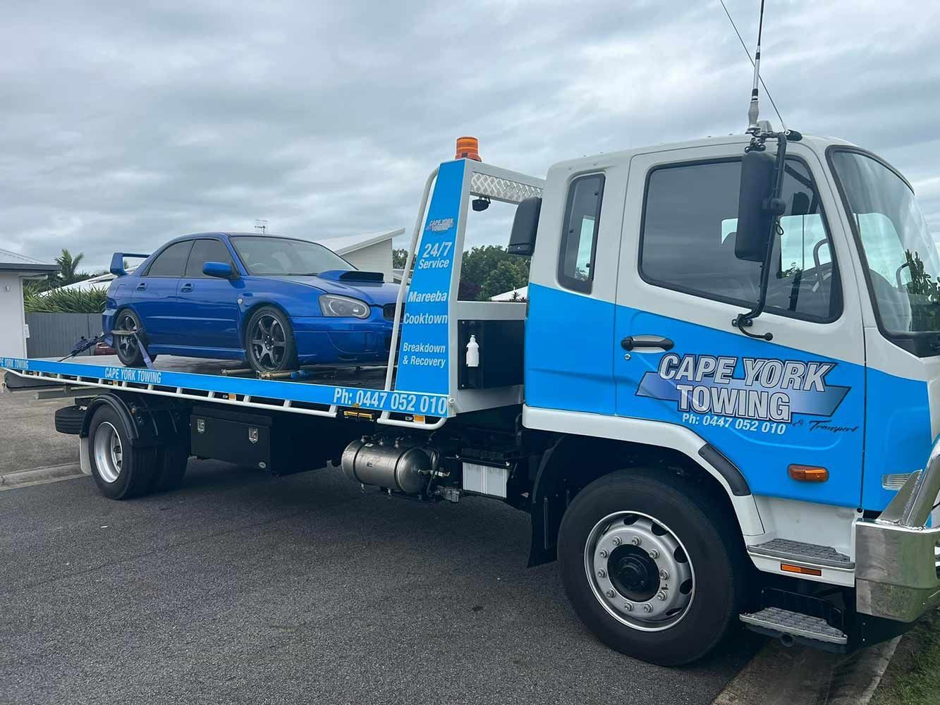 Blue tow truck carrying a blue car parked roadside — Cape York Towing in Lockhart River, QLD