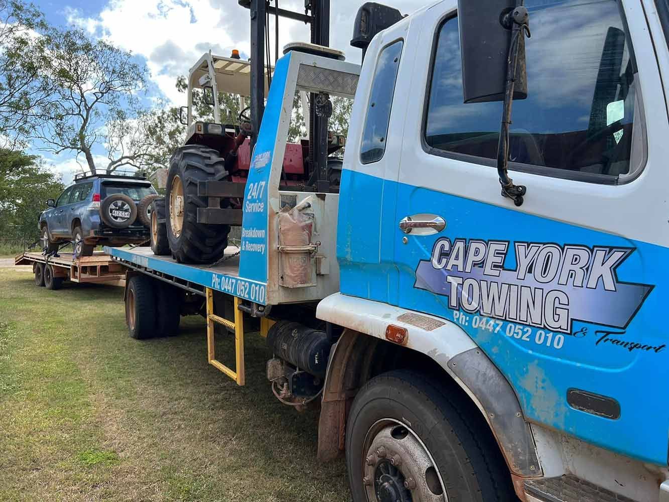A Blue and White Towing Truck is Carrying a Tractor and a Car — Cape York Towing & Transport in Lockhart River, QLD