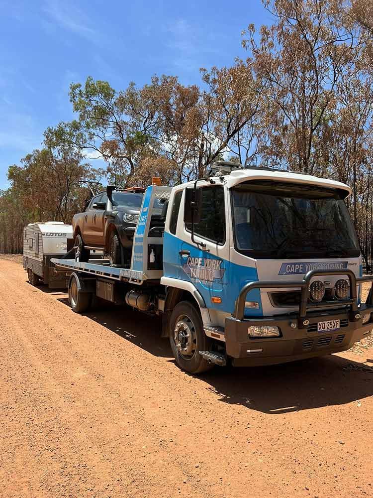 A Tow Truck is Carrying a Car and a Trailer on a Dirt Road — Cape York Towing & Transport in Mount Molloy, QLD