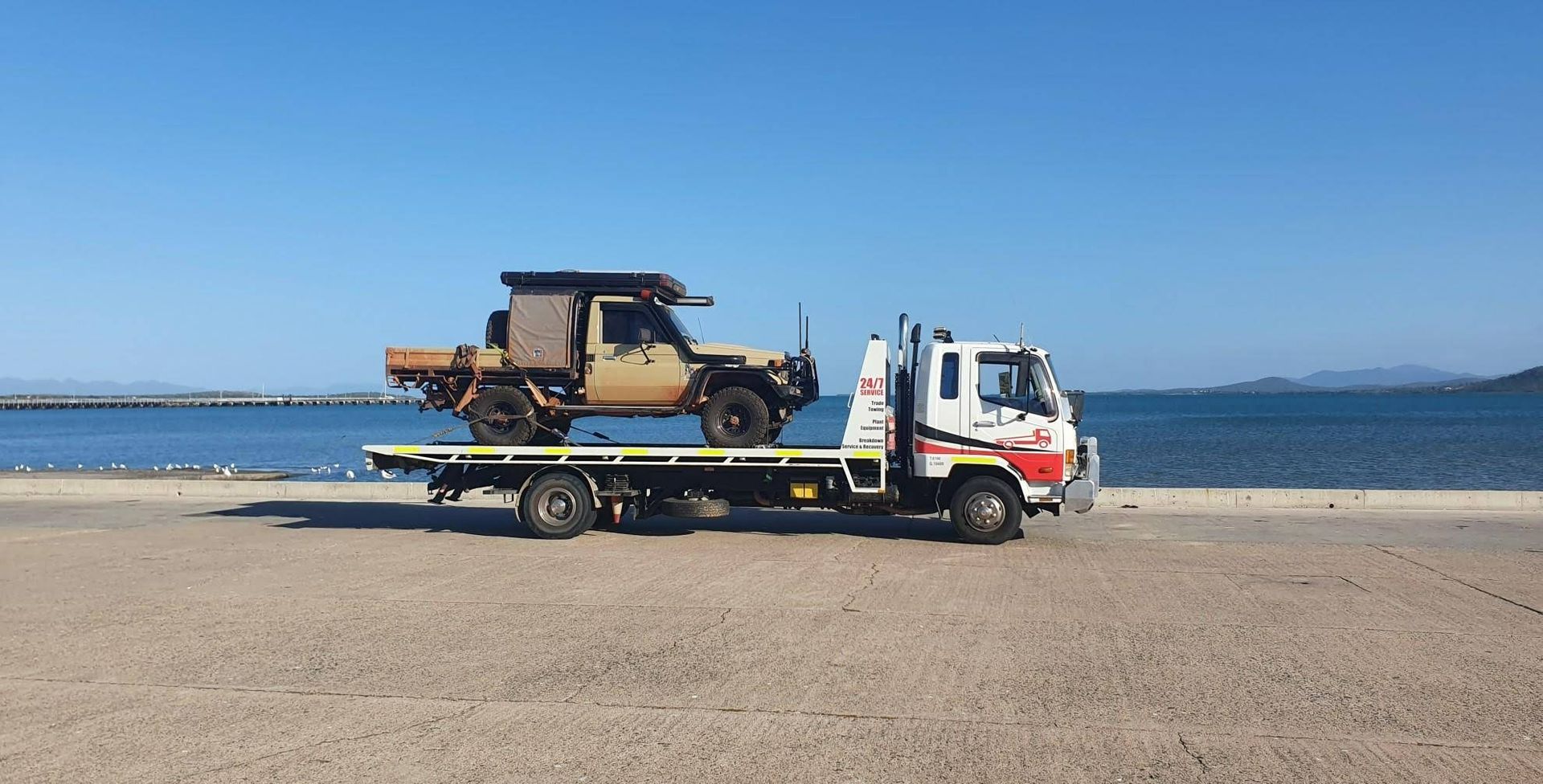 A Tow Truck is Carrying a Jeep on the Back of It on a Beach — Cape York Towing & Transport in Brisbane, QLD
