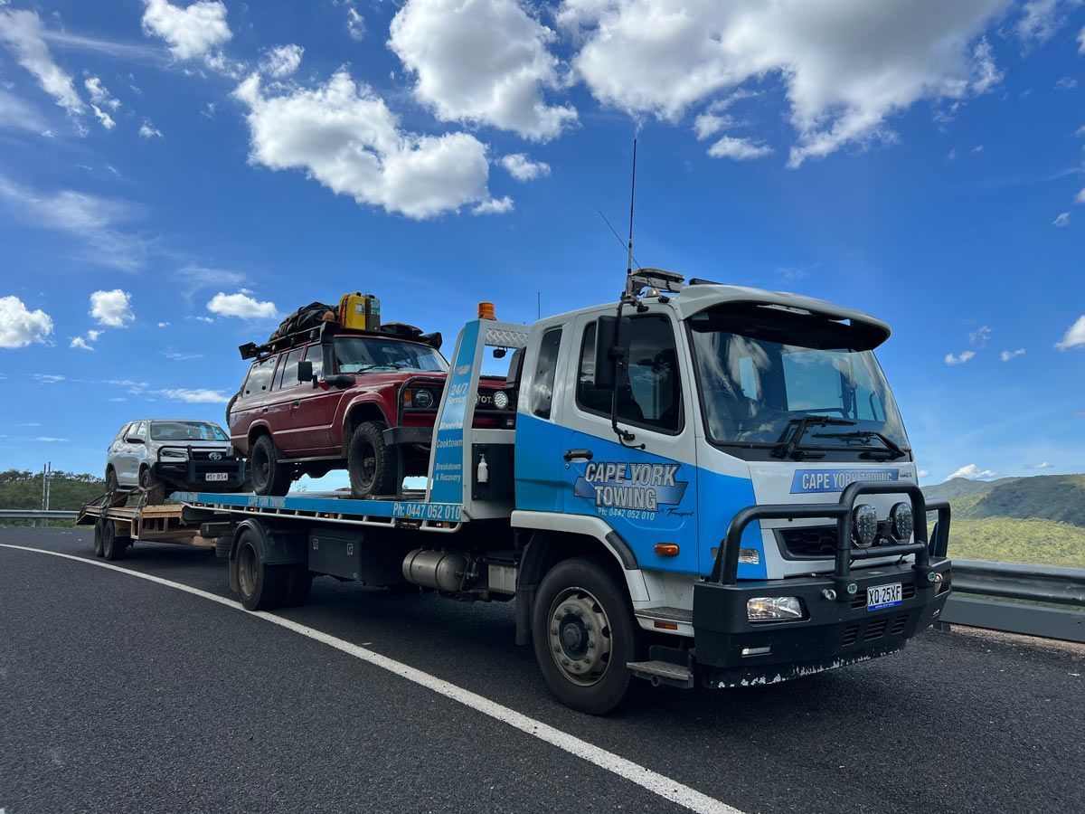 A Tow Truck is Carrying Two Cars on a Trailer on a Highway — Cape York Towing & Transport in Mareeba, QLD