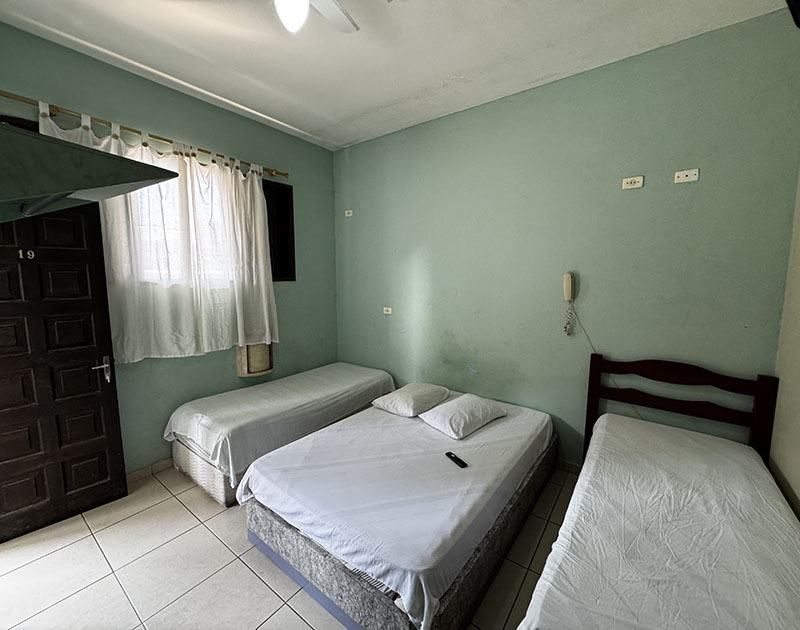 Um quarto com paredes verde-menta, piso de azulejo claro, uma cama de casal e duas camas de solteiro com lençóis brancos.