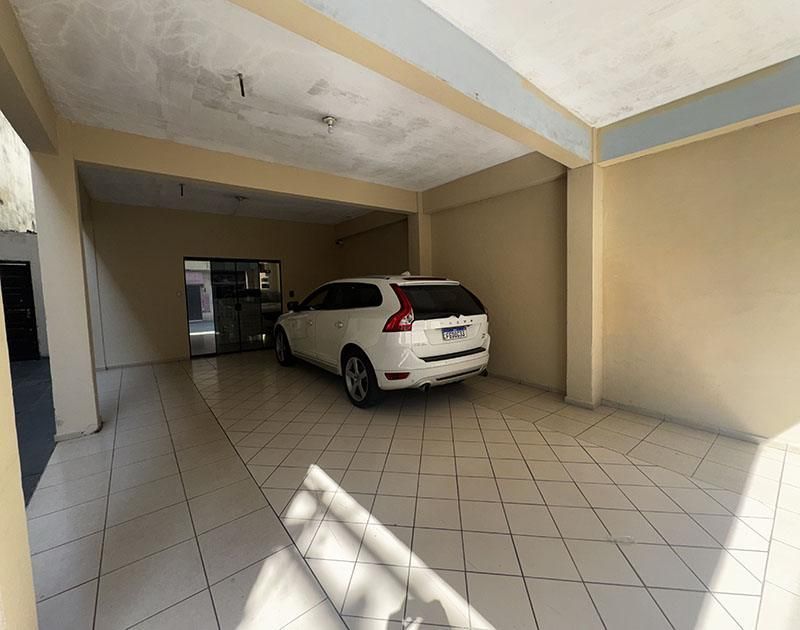 Um SUV branco está estacionado em uma garagem coberta com piso de azulejo, sob a cobertura de um prédio.